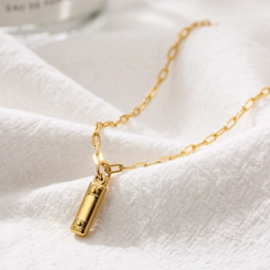 Macro shot of gold rectangular pendant necklace with rivet detail on white fabric