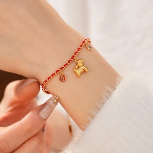 Macro detail of red string bracelet featuring 18K gold plated PiXiu and coin pendants