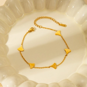 Macro shot of gold fan charms on a stainless steel bracelet over a white tray