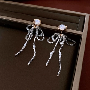 Detail of 18k gold plated bow earrings with crystal studs and hanging pearl tassels