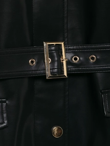 Detail der schwarzen Kunstlederjacke mit goldener Schnalle und verstellbarem Taillengürtel