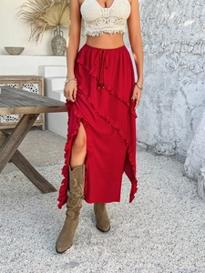 Detail of red long skirt featuring ruffle trimming, a high side slit, and drawstring waist