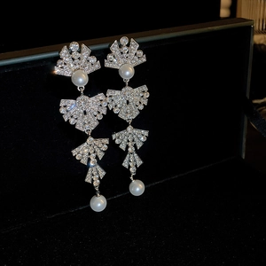 Silver bow dangle earrings with sparkling rhinestones and white pearls on black box