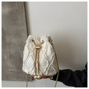 Detail of white canvas bucket bag featuring frayed edges and elegant pearl drawstring