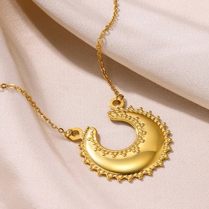 Vue détaillée du pendentif lune doré avec bordure perlée sur un tissu en soie