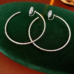 Dettaglio di orecchini a clip tondi placcati oro su un cuscino di velluto verde