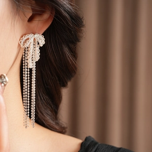 Close-up of silver bow tassel earrings with sparkling rhinestones worn by a model