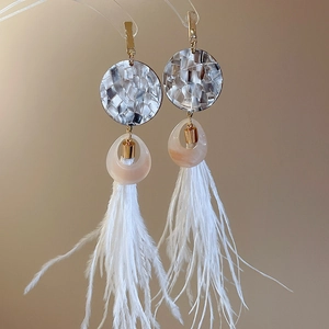 Détail montrant les longs pompons en plumes blanches et la résine texturée des boucles d'oreilles