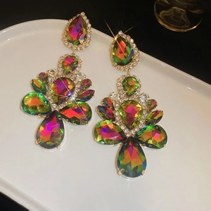 Detail of oversized gold teardrop earrings with multi-color crystals on a white plate