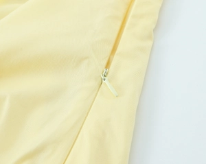 Dettaglio macro della cerniera invisibile e cuciture fini sul top in popeline giallo