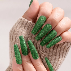 Detailed close-up of long green glitter false nails worn with a beige knitted sweater