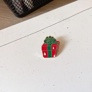 Detailed close-up of a Christmas gift box enamel pin with red and green festive colors