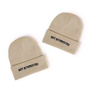 Khaki beanie hat with black Not Interested embroidery in a minimalist streetwear style