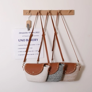 Three stylish straw crossbody bags with brown PU flap and rivets hanging on hooks