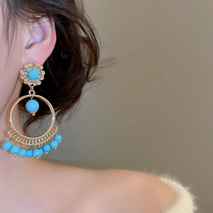 Detail of ethnic gold hoop earrings with turquoise beads and tassels worn by a model