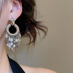 Close-up of geometric round silver earrings with layered sequin fringe on a model