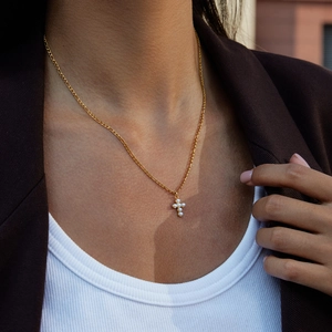 Dettaglio della collana a croce in acciaio dorato con perle sul collo della modella