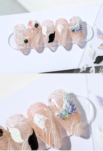 Macro detail of 3D angel wing nail stickers with pearls and glitter on nude pink base