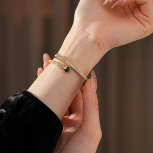 Detail of gold-plated bangle with green gemstone and pavé-set stones on wrist