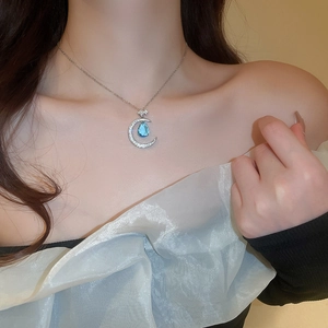 Close-up of elegant crescent moon necklace with blue teardrop zircon on woman's neck