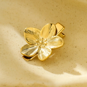 Elegant gold metal flower hair clip with petal texture on a textured beige ceramic plate