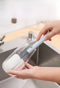Deep cleaning of a glass using a long-handled blue sponge brush in a kitchen sink