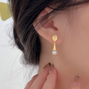 Close-up of elegant gold cone and white pearl drop earrings worn by a model