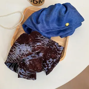 Vintage navy beret with metal buckle and patterned fabric accessory on a wooden tray