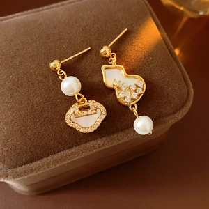 Close-up of asymmetric gold earrings with zircon, mother of pearl and pearls on velvet