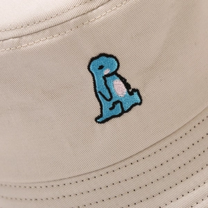 Close-up of blue dinosaur embroidery and stitching on beige cotton bucket hat