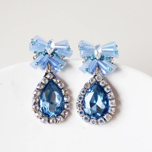Detailed close-up of blue crystal bow and teardrop pendant earrings with silver settings