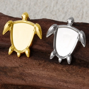 Detailed close-up of turtle stud earrings in gold and silver finish on a wooden background