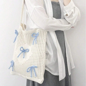 Chic cream-colored knitted shoulder bag with blue bow details and hollow design on model