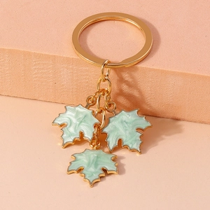 Close-up of light green enamel maple leaf charms on a golden keychain with a pink backdrop