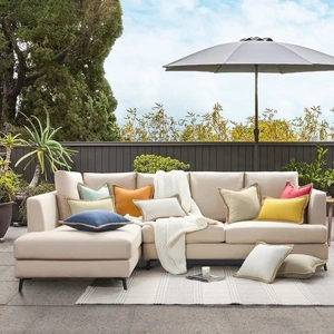L-shaped sofa with colorful linen cushion covers featuring braided edge trim in a patio setting