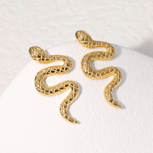 Macro shot of gold snake-shaped stud earrings with detailed scale texture on white stand