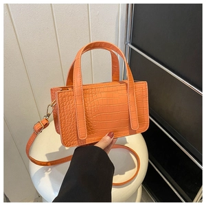 Detailed view of orange crocodile pattern on small square handbag with handle and strap