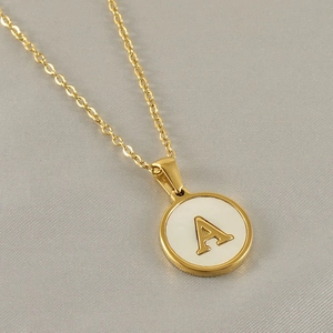 Macro shot of gold 18k necklace with letter A engraved on a white mother of pearl pendant