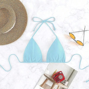 Flat lay detail of a light blue tie-front bikini top on marble background with beach props