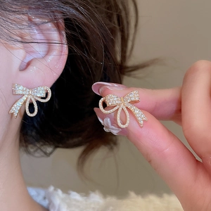 Detail showing the gold bow earrings with cubic zirconia worn by a person on ear