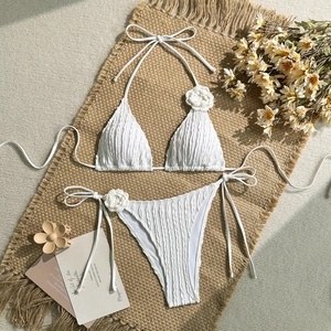 Close-up of white bikini with 3D floral accents and textured fabric on jute background