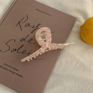Detailed view of pink marble acetate hair claw clip on soft fabric and book background