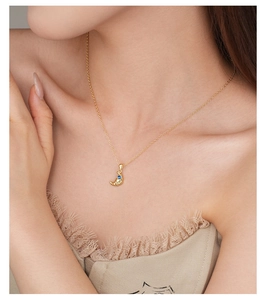 Close-up of a gold croissant pendant necklace with a blue gemstone on a woman neck