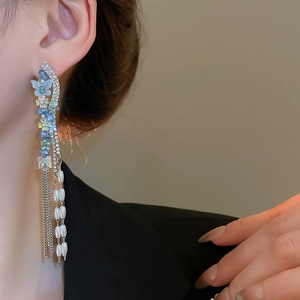Close-up of butterfly earrings with blue crystals, silver tassels and white pearls
