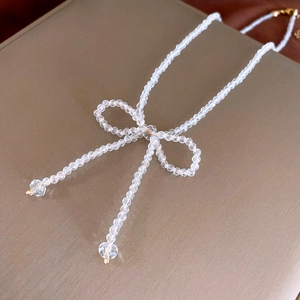 Detail shot of a crystal bead bow necklace on a textured champagne gold metal stand