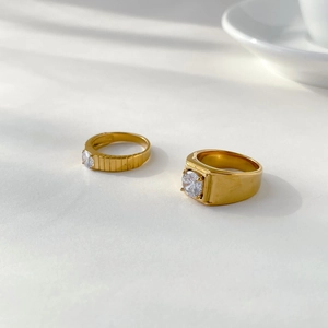 Detail view of two gold couple rings with one-carat round gemstones and gear-textured bands