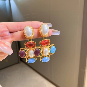 Détail de boucles d'oreilles rétro avec perle ovale et breloques de croix en pierres colorées