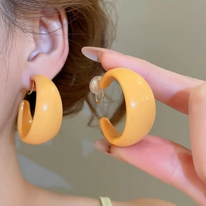 Macro detail of bright orange C-shaped acrylic hoop earrings on ear for pop retro style