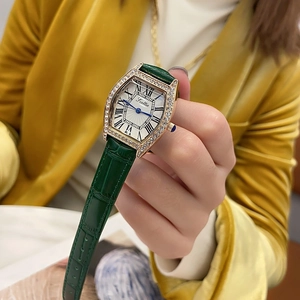 Close-up of a tonneau-shaped gold watch with diamonds and green crocodile leather strap
