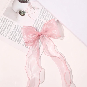 Detail view of pink organza bow hair clip with flowing ribbons on white table